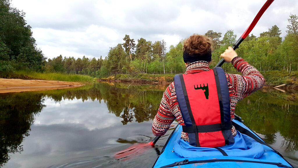 Meloja kanootissa selkäpuolelta kuvattuna. Punaisiin pelastusliiveihin lisätty museon logo.